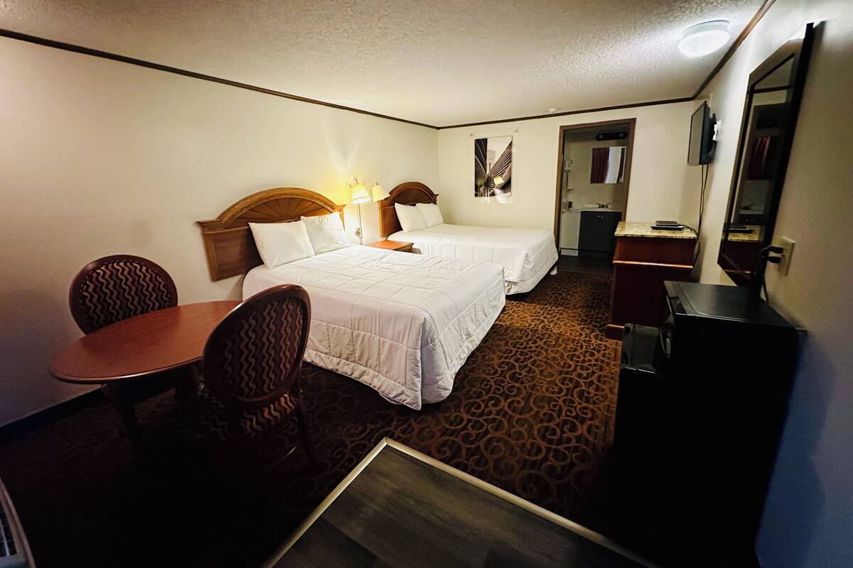 A hotel room with two beds, a desk, a chair, a television, and a bathroom visible through an open door.