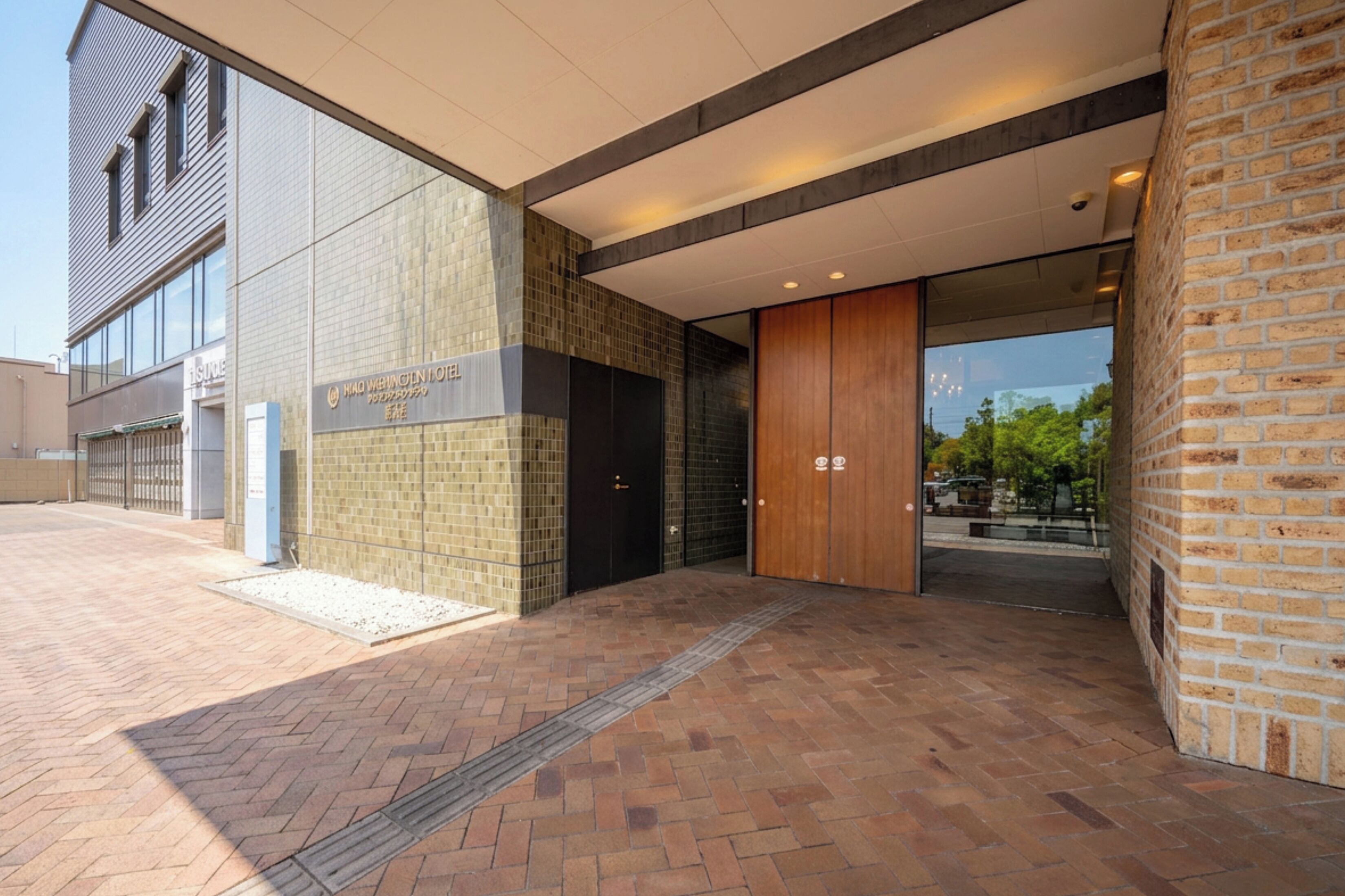 Een modern gebouwde ingang met een bakstenen gevel, een glazen deur en een bord waarop een hotel wordt aangegeven.