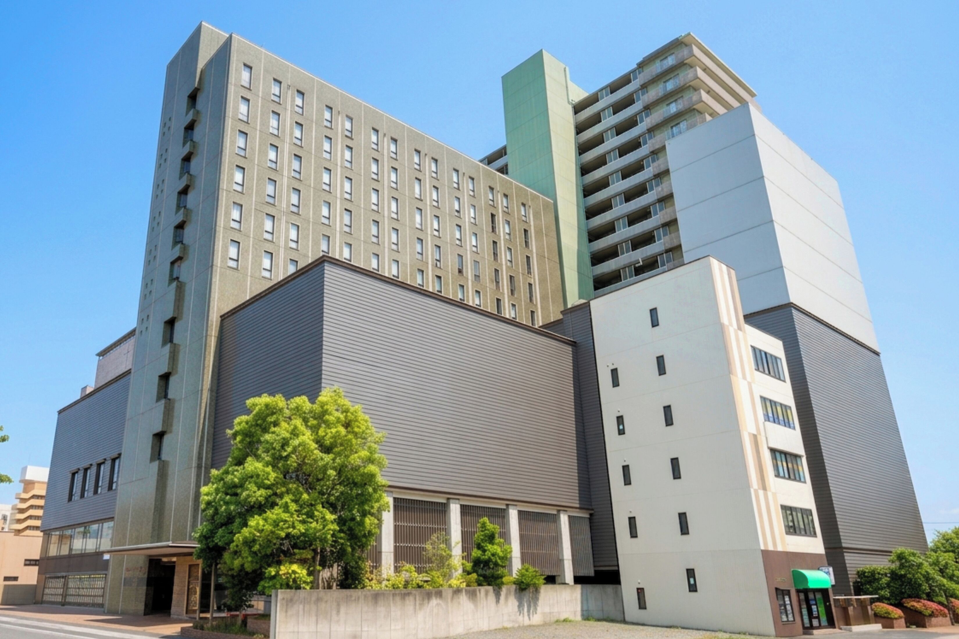 Een hotel met meerdere verdiepingen, met een modern architectonisch ontwerp, een opvallende ingang en een grote boom op de voorgrond.