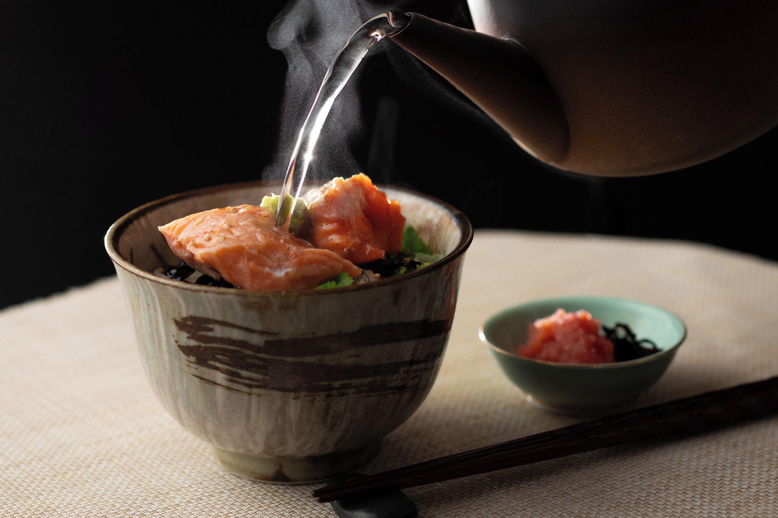 A bowl of food with chopsticks and a teapot.