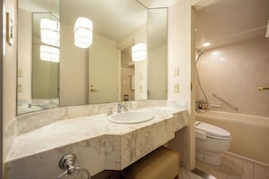 Un baño con lavamanos de mármol, un espejo grande, inodoro y zona de ducha.