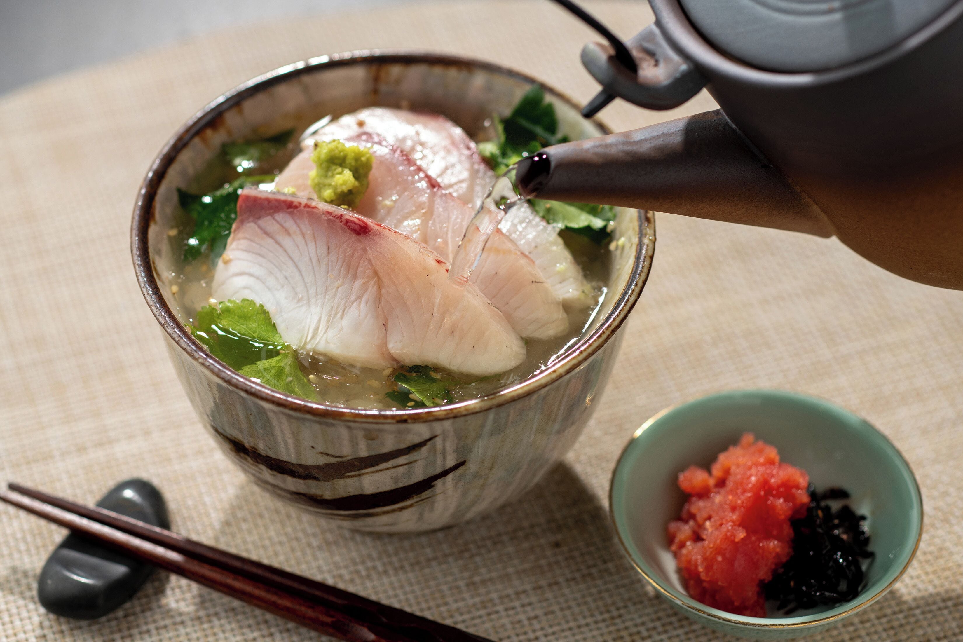 A bowl of soup with chopsticks and a teapot.