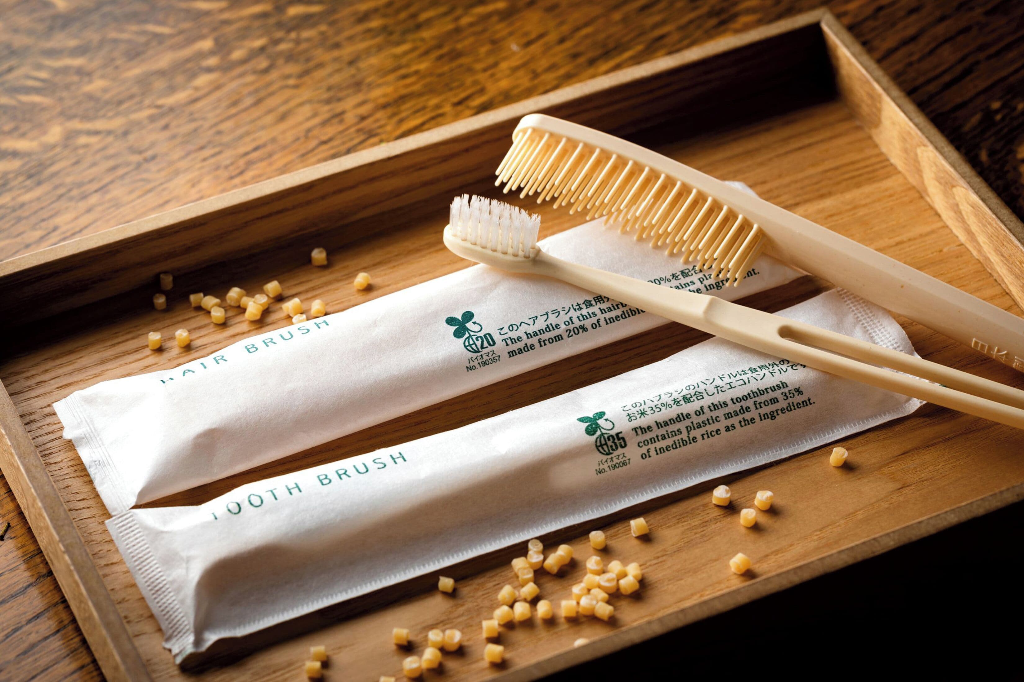 Uma bandeja de madeira com duas escovas de dentes e dois pacotes de 'Hair Brush' e 'Tooth Brush' sobre uma superfície de madeira.