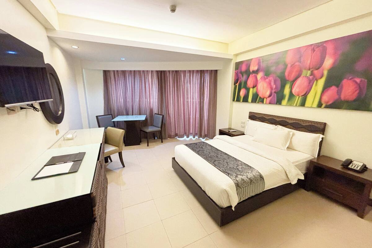 Een hotelkamer met een bed, bureau, stoel en een bloemen schilderij.