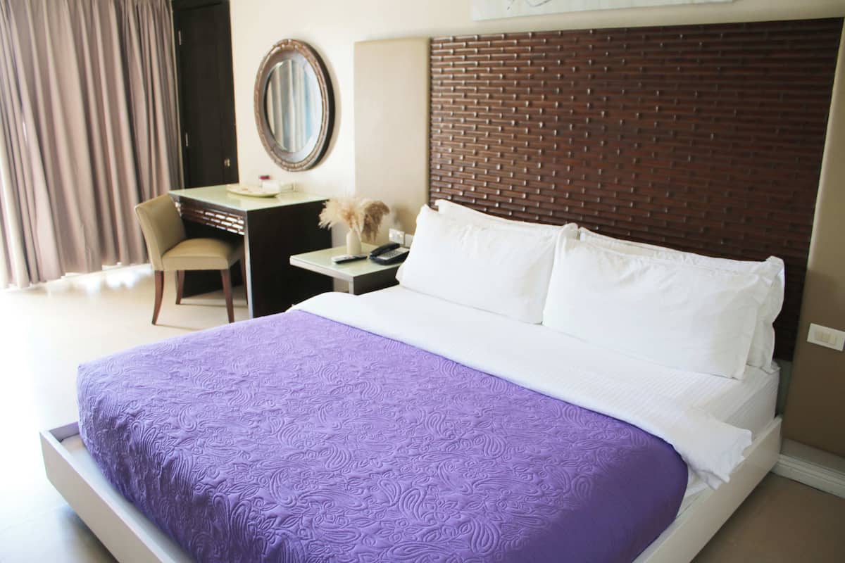 Hotelkamer met een groot bed, een bureau met stoel, een spiegel en een hoofdeinde met baksteenmotief.