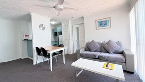 A modern living room with a grey sofa, a white coffee table, and a dining area with a wooden table and black chairs. - Santana Resort (Surfers Paradise)
