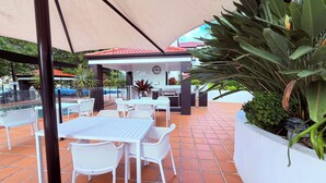 An outdoor patio area with white tables and chairs, a covered seating area, and a pool in the background. - Santana Resort (Surfers Paradise)