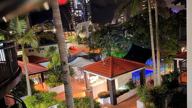 A rooftop terrace with outdoor seating, palm trees, and a view of a cityscape at night. - Santana Resort (Surfers Paradise)
