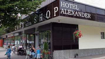 A building with a sign reading "HOTEL ALEXANDER" and a visible storefront with the name "CAFE ALEXANDER".