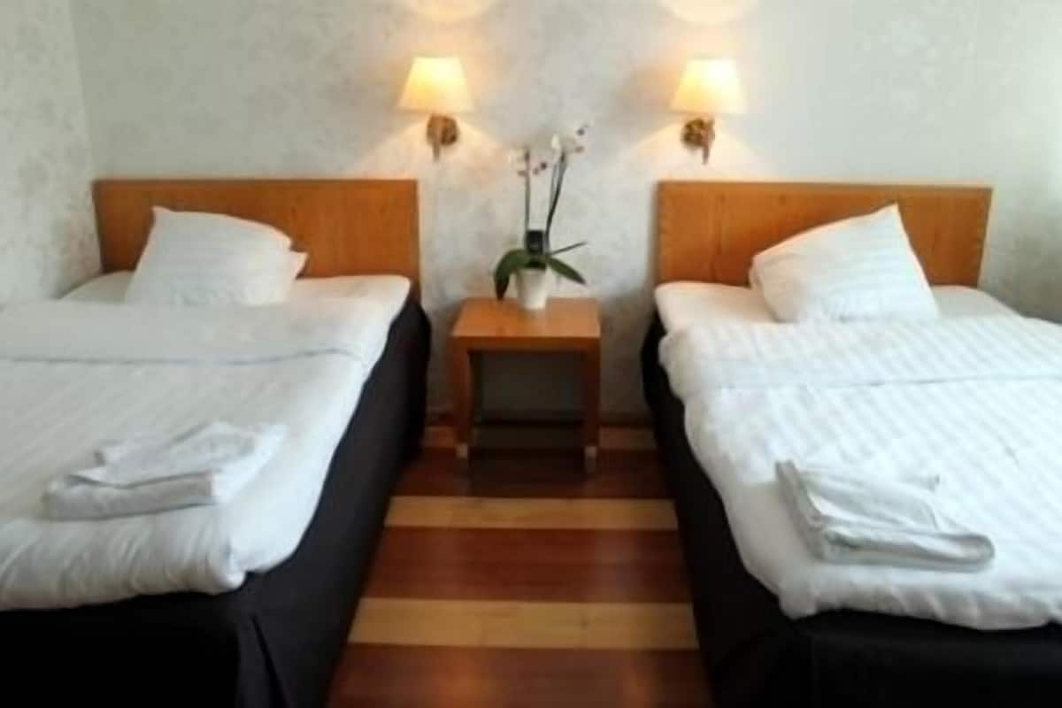 A hotel room with two single beds, a wooden nightstand between them, and a small table with a lamp.