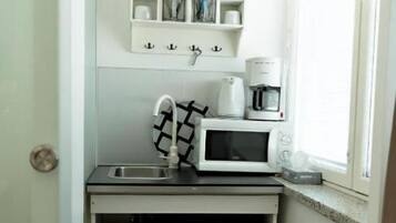 Une cuisine compacte équipée d’un four à micro-ondes, d’une machine à café et d’un petit évier.