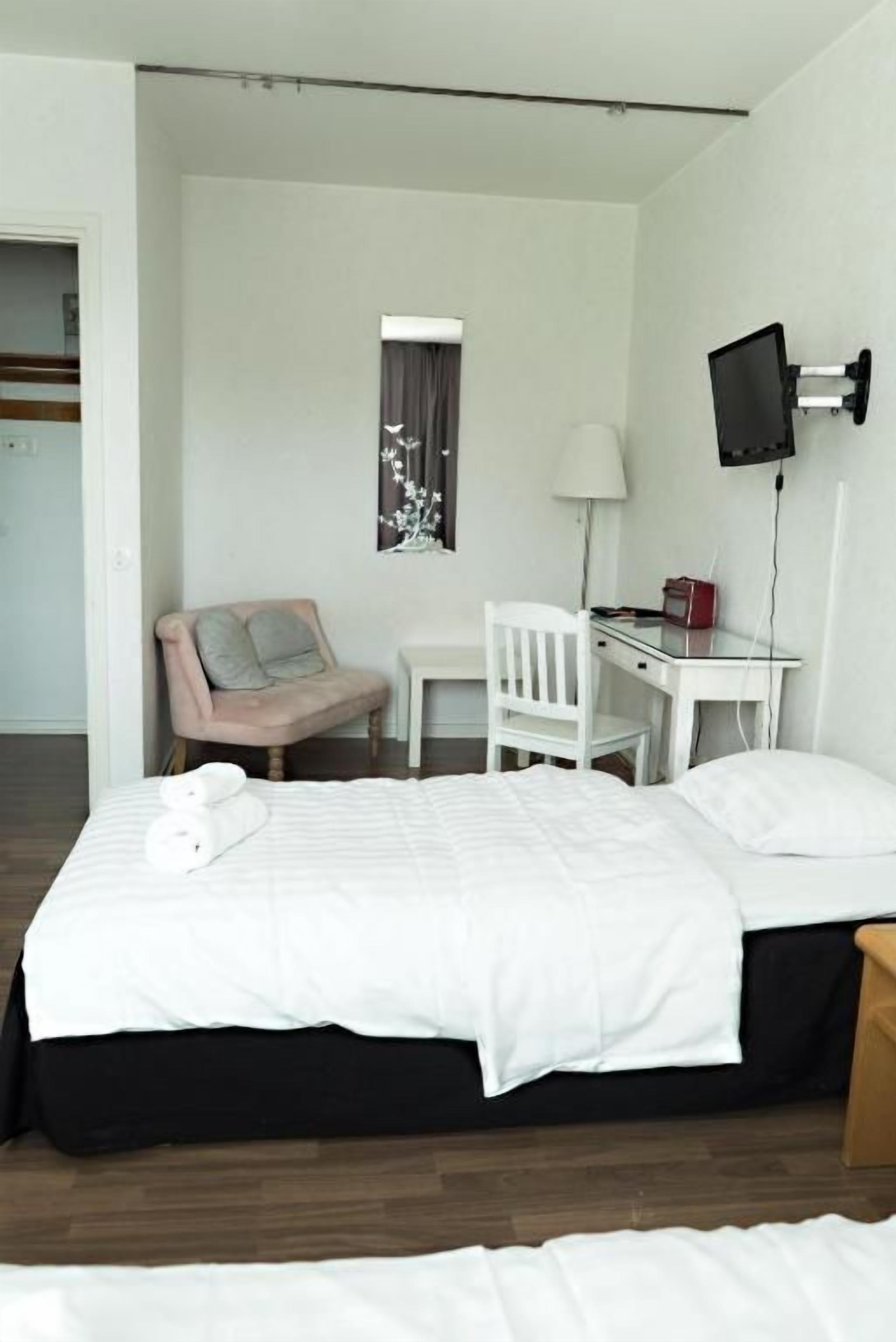 Hotellihuone, jossa on sänky, työpöytä, tuoli, televisio ja ikkuna, jossa on verhot.