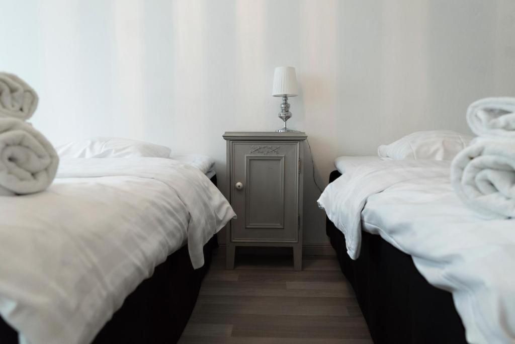 A hotel room with two beds, a nightstand with a lamp, and towels.