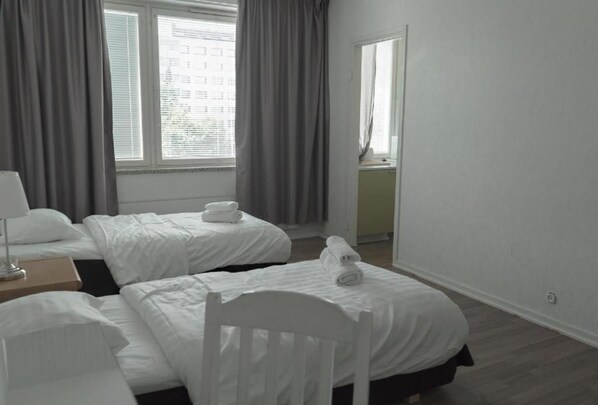 A hotel room with two beds, a chair, a nightstand, and a window with curtains.