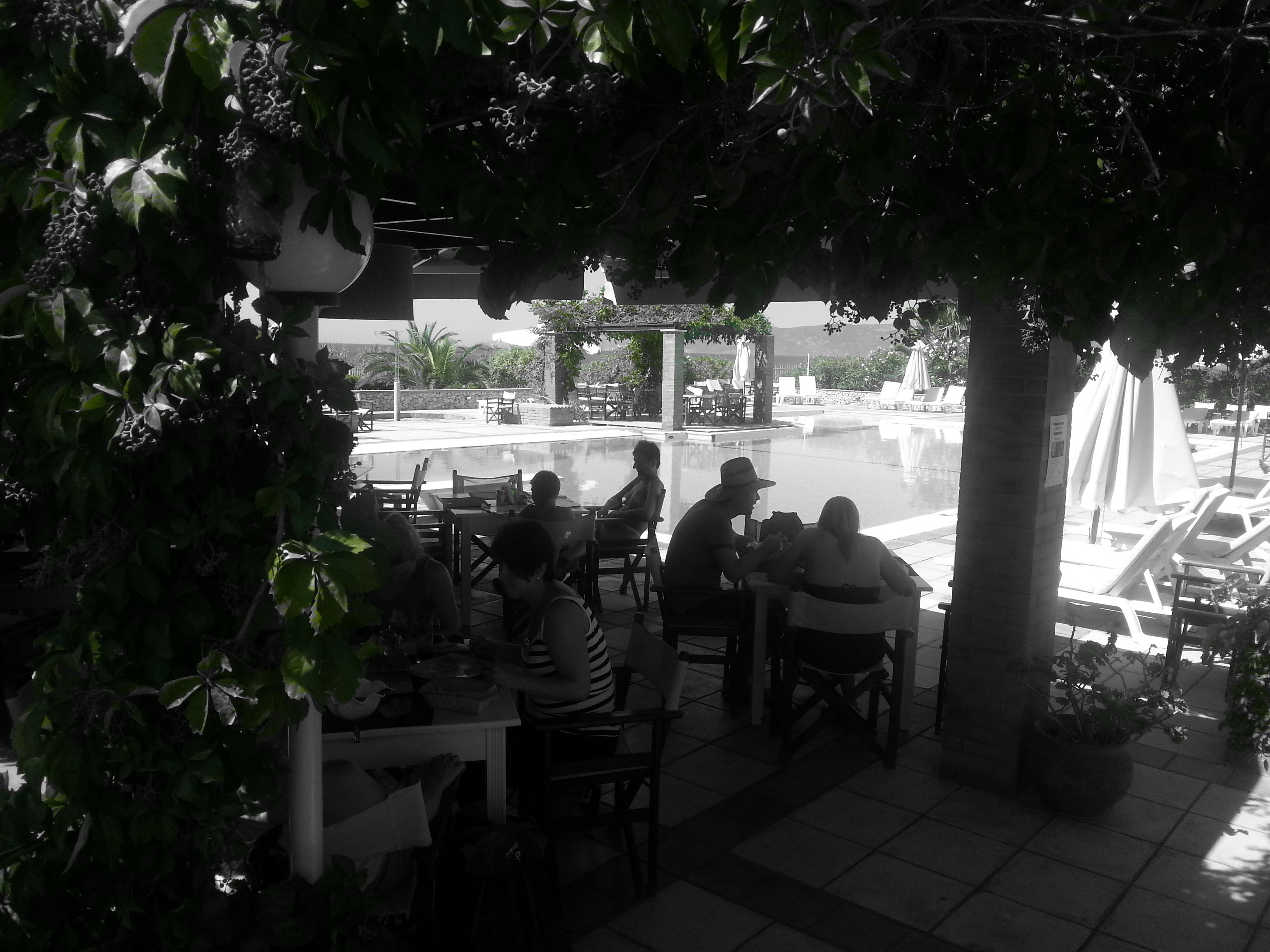 Ein Außenbereich mit Essbereich, Tischen, Stühlen, einem Pool und einem Springbrunnen im Hintergrund.