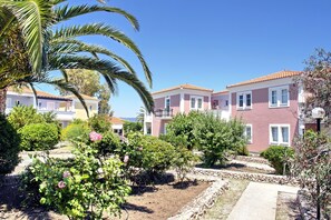 A residential area with a row of pink houses, a palm tree, and a garden with roses. - Panselinos Hotel (Lesvos)