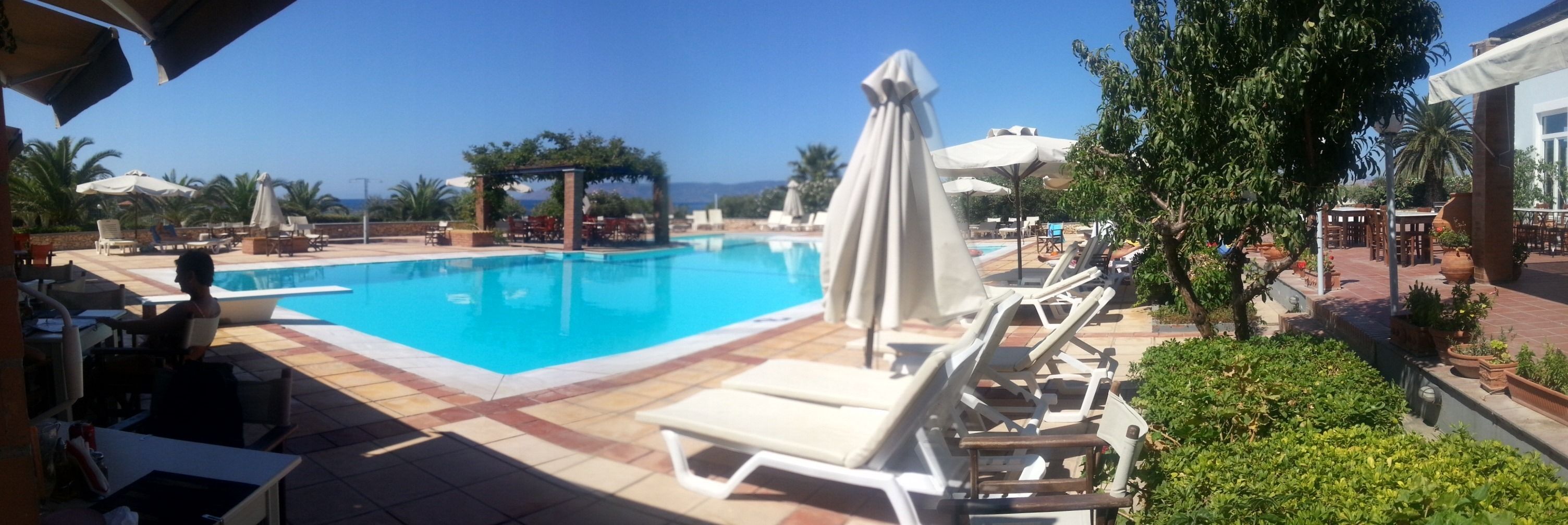 Un área de piscina con sillas de descanso y sombrillas, rodeada de vegetación y vistas al mar.