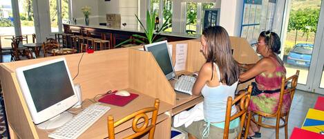 Un laboratorio de computación con escritorios y sillas de madera, computadoras y vistas al exterior a través de amplios ventanales.