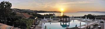 Un resort con piscina, sillones de descanso y vista al atardecer sobre el mar.