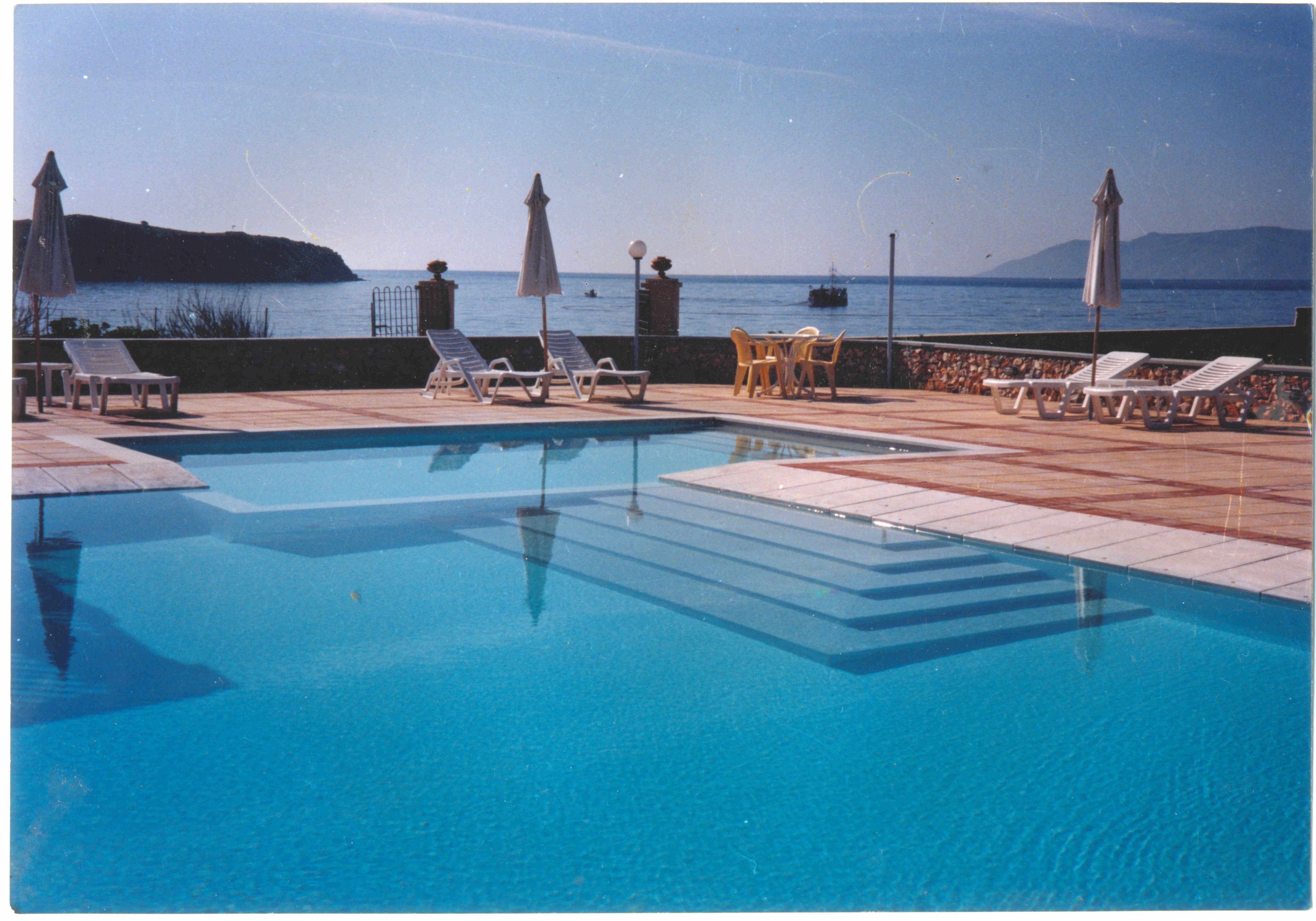 A swimming pool with lounge chairs and umbrellas, overlooking a body of water with boats.