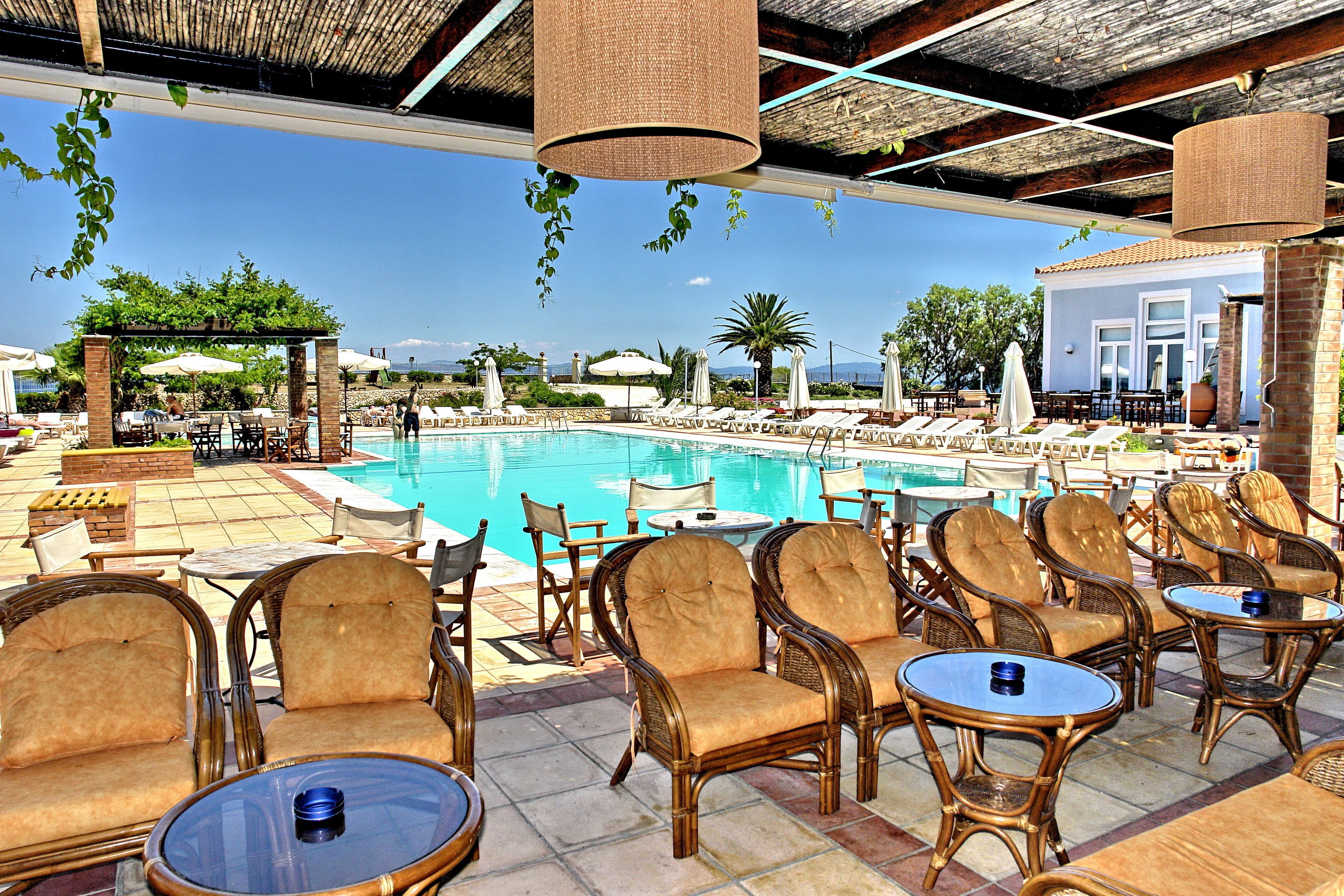 A poolside area with lounge chairs and tables, a clear pool, and a building in the background.