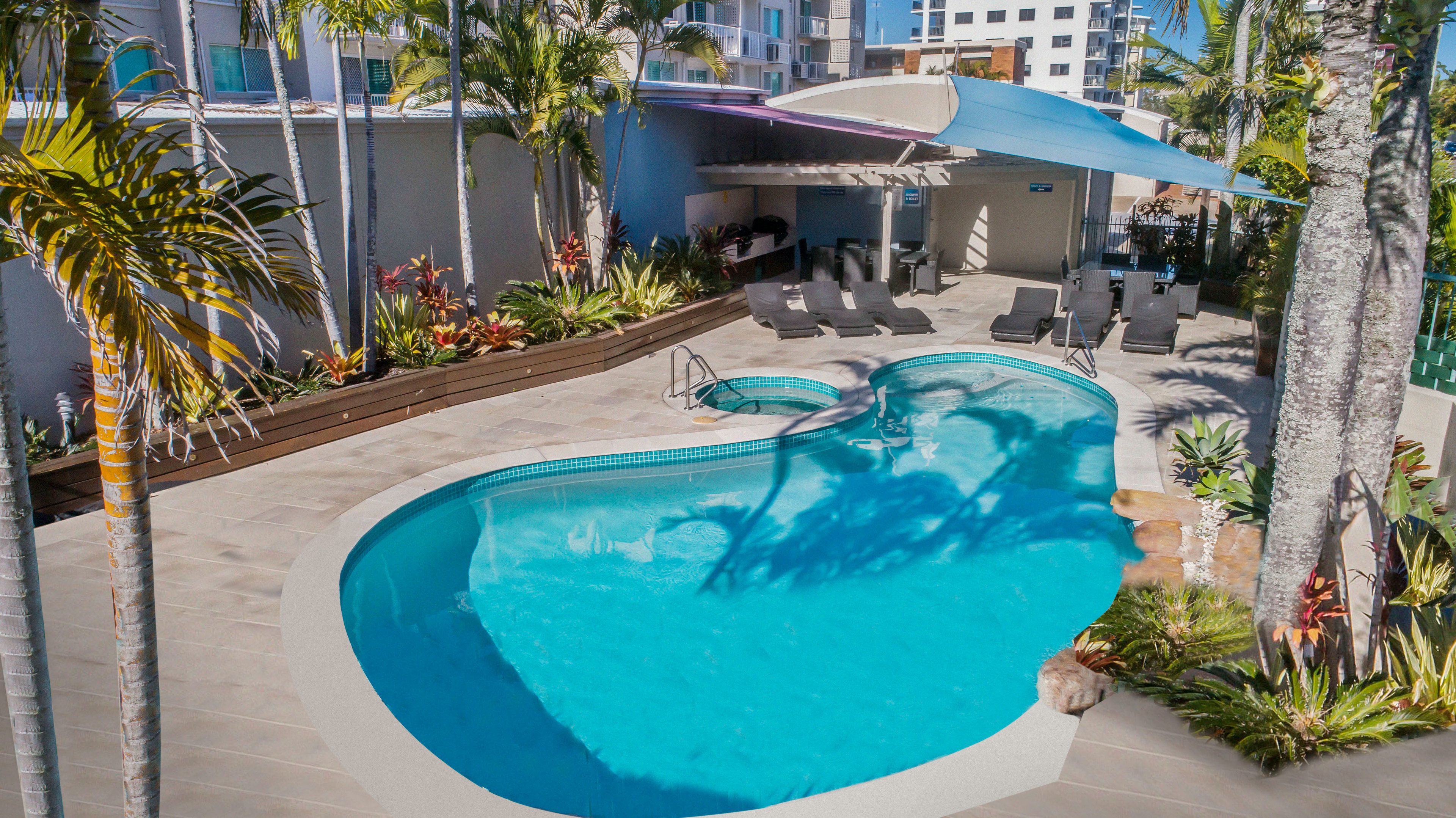 Ein Swimmingpool mit Sonnenschirm, umgeben von Palmen und Liegestühlen.