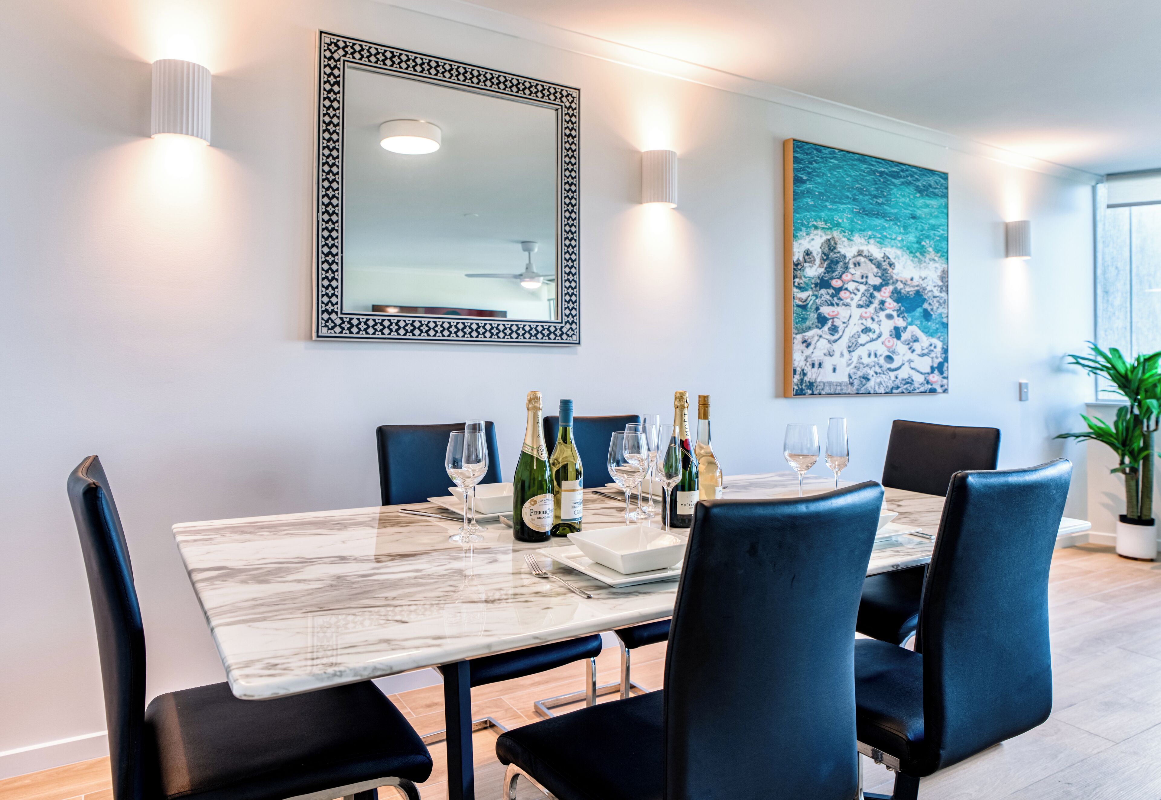 A dining area with a marble table, black chairs, and a large mirror on the wall.