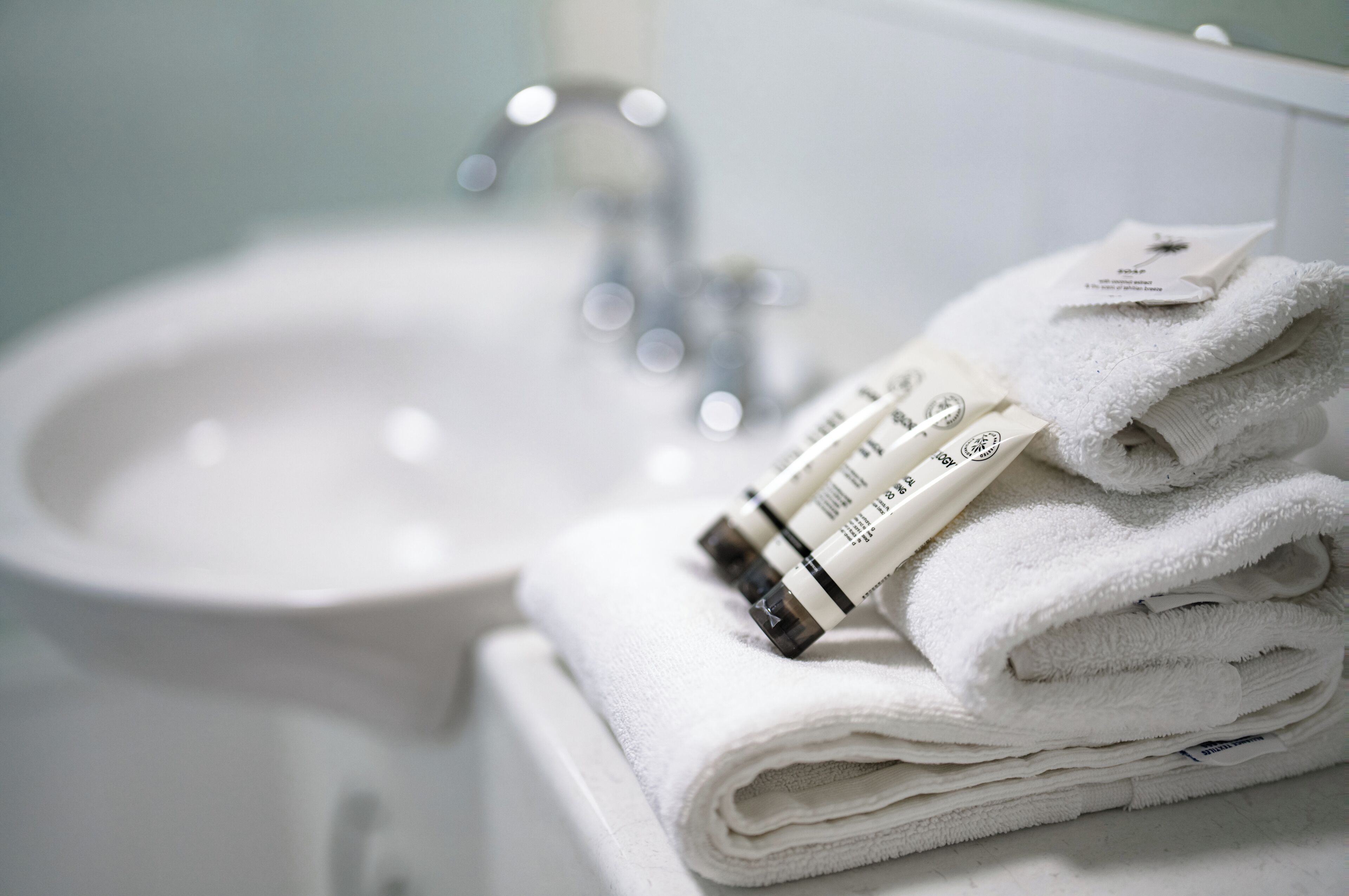 A bathroom with a white sink and stacked white towels.