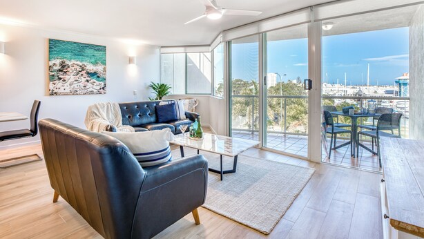 A modern living room with a leather sofa, a coffee table, and a view of the marina through large windows.