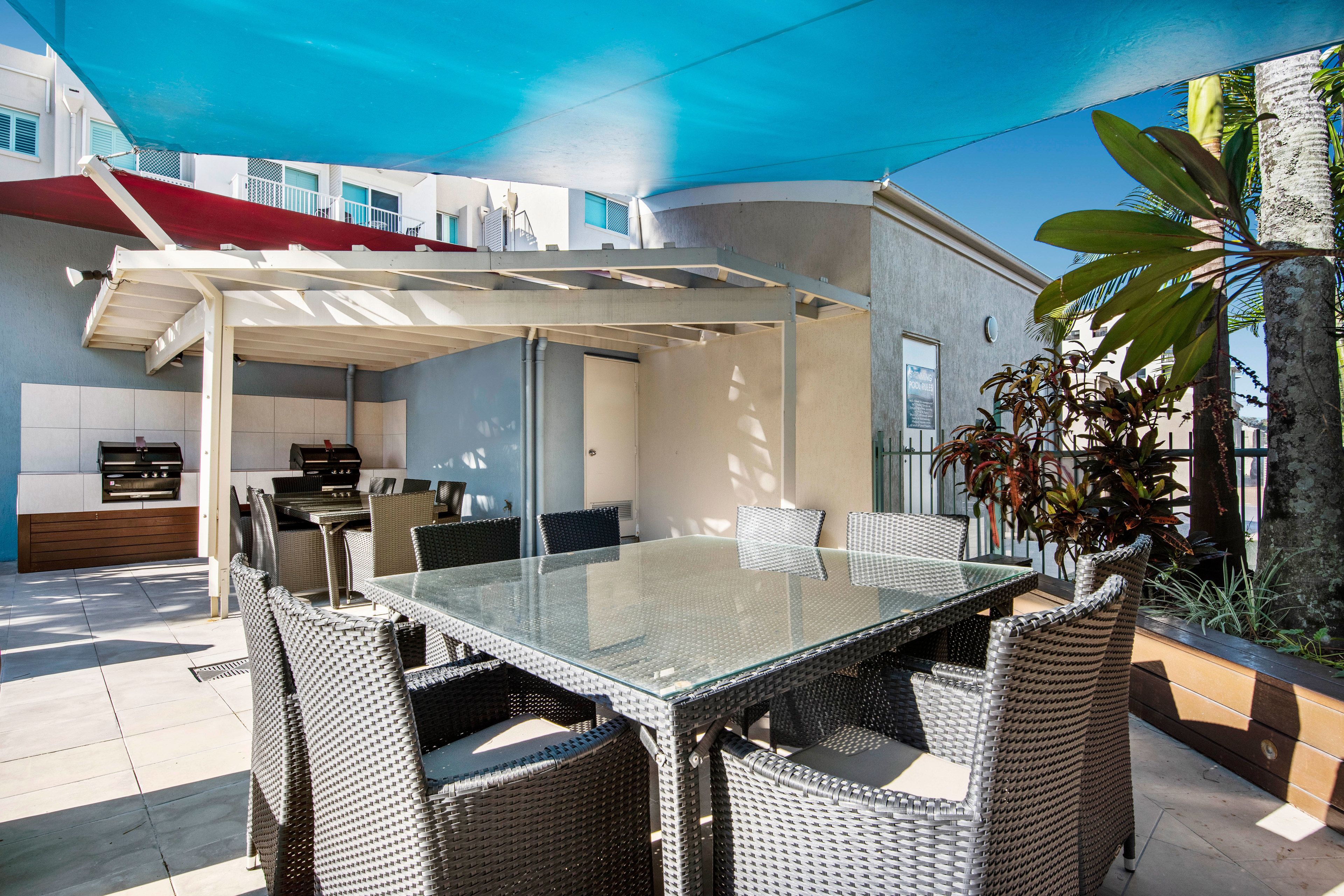 An outdoor patio with a glass-top table and wicker chairs, a barbecue grill, and a covered seating area.