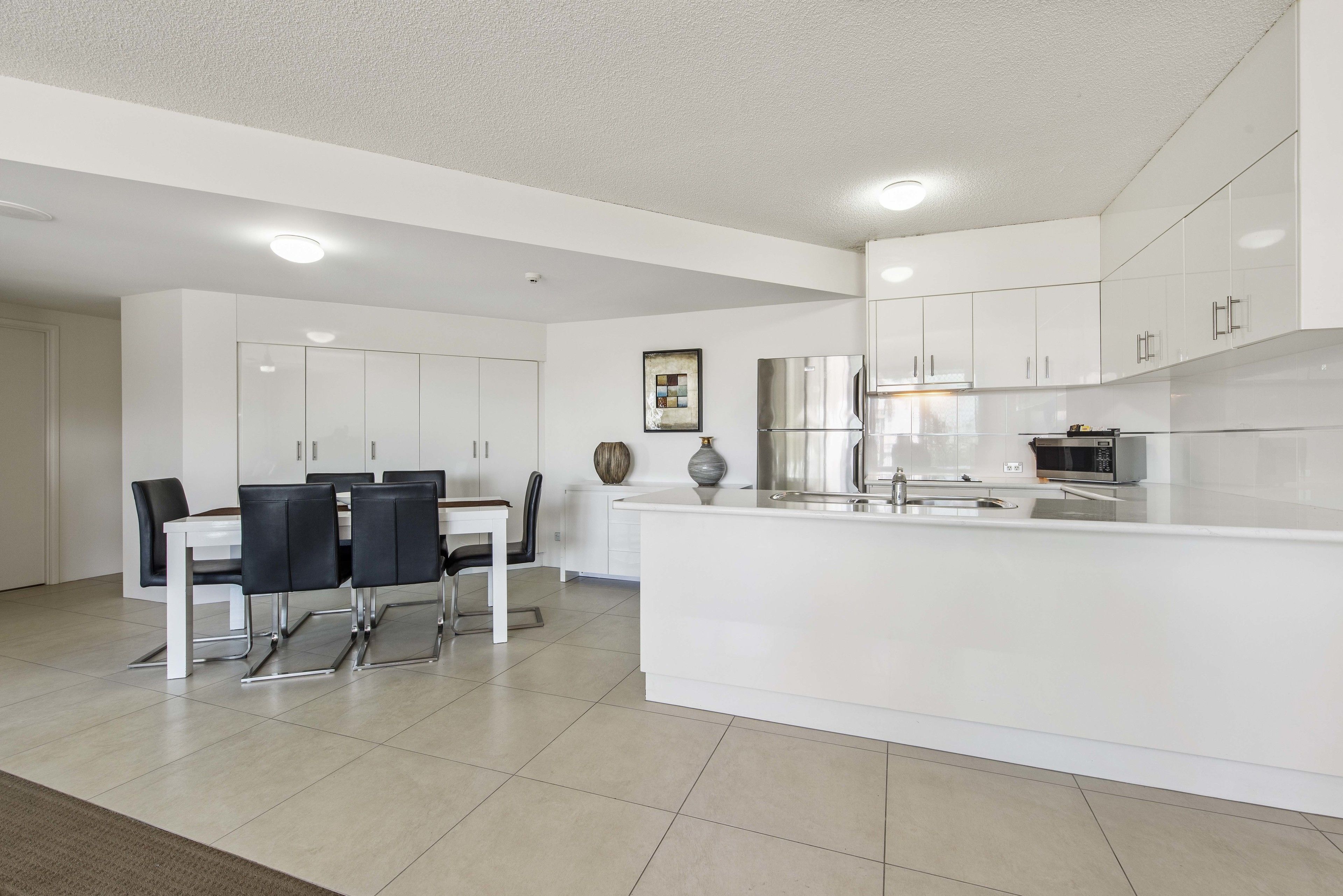 A modern kitchen with white cabinetry, a central island, and a dining area with a table and chairs.
