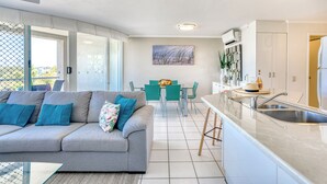 A modern living room with a grey sofa, teal chairs, and a glass coffee table.