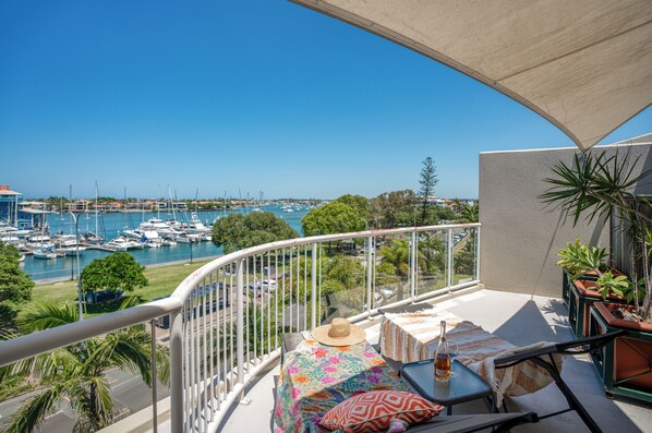 A balcony with a view of a marina, a table with a bottle and glasses, and a potted plant.