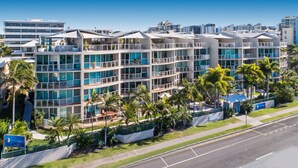 Un hotel de varios pisos con balcones, mesas al aire libre y palmeras.