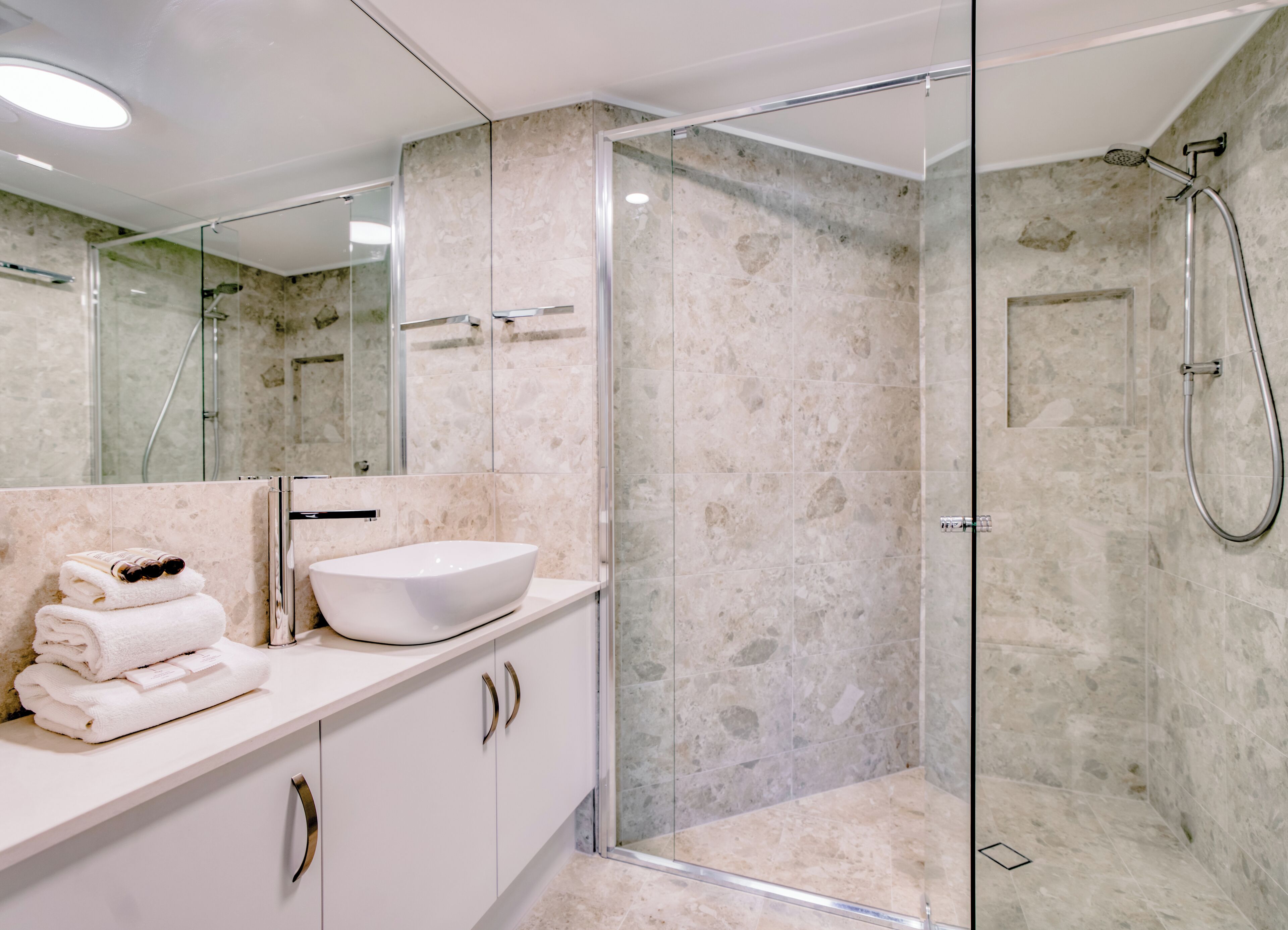 A modern bathroom with a glass-enclosed shower, a white sink, and a marble-tiled wall.