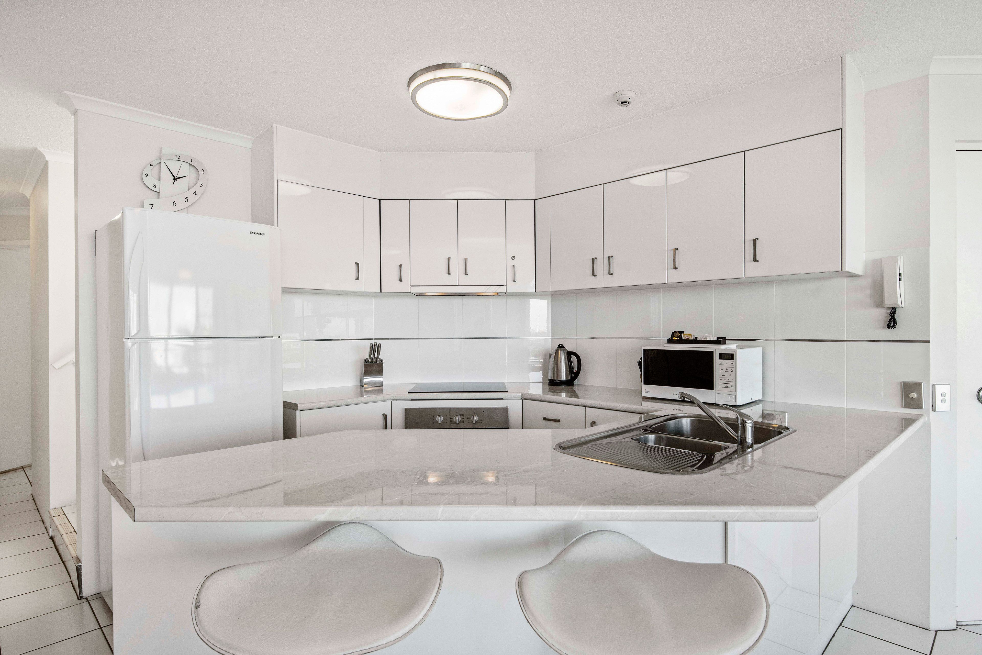 Una cocina moderna con armarios blancos, horno empotrado, microondas y pileta de acero inoxidable.