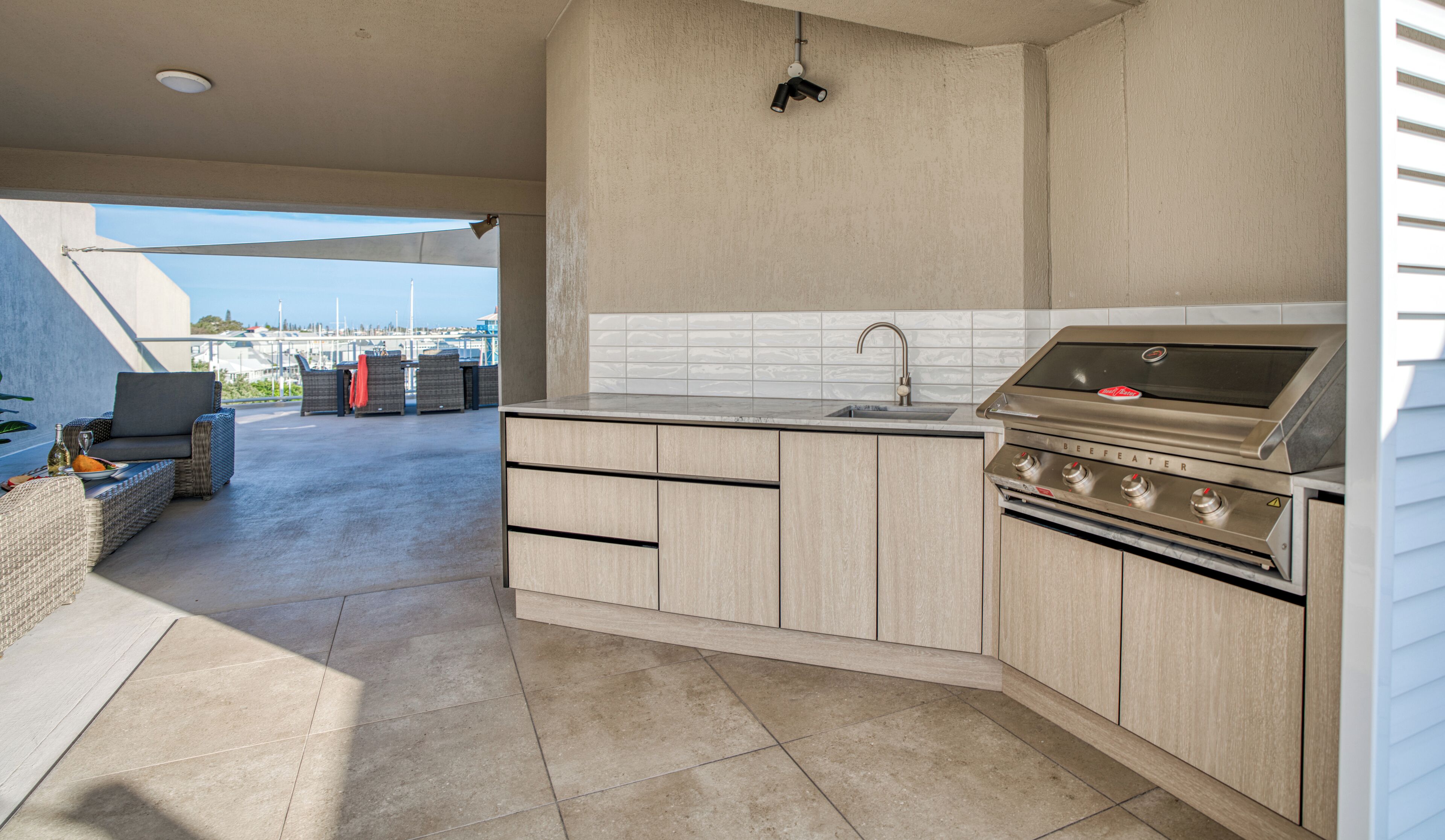 Een moderne keuken met een ingebouwde grill, een spoelbak en een eethoek met buitenmeubilair.