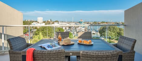 A balcony with wicker furniture, a table with a newspaper, a bottle, and a plate of oranges.