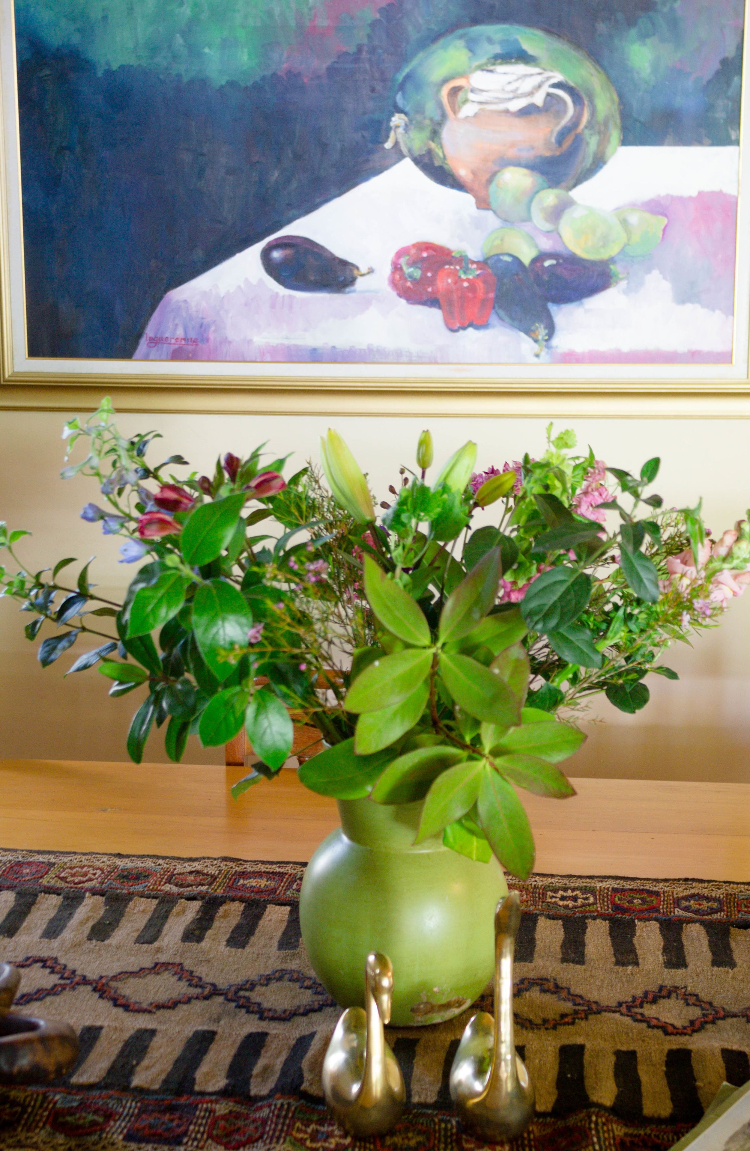 Un vase vert avec une plante, posé sur un tapis à motifs.