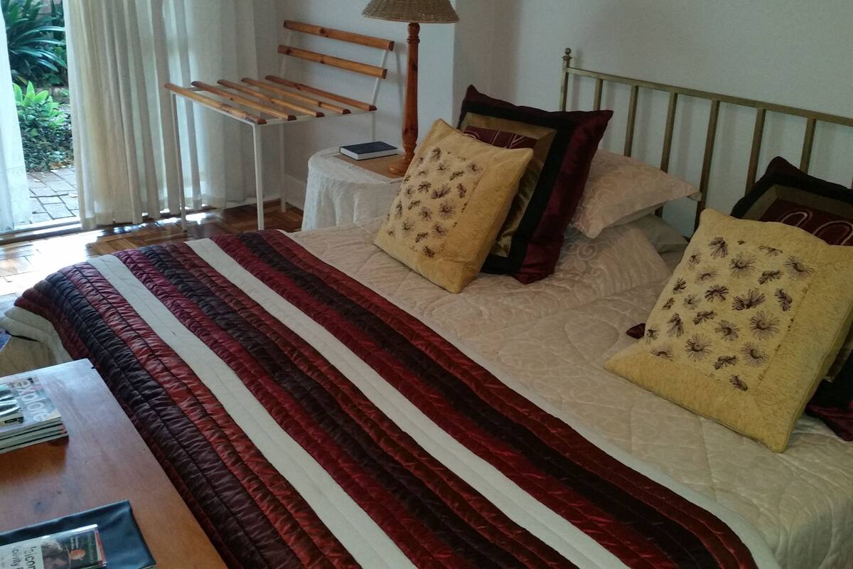 A neatly made bed with a striped bedspread, a bedside lamp, and a small table with a book and a magazine.