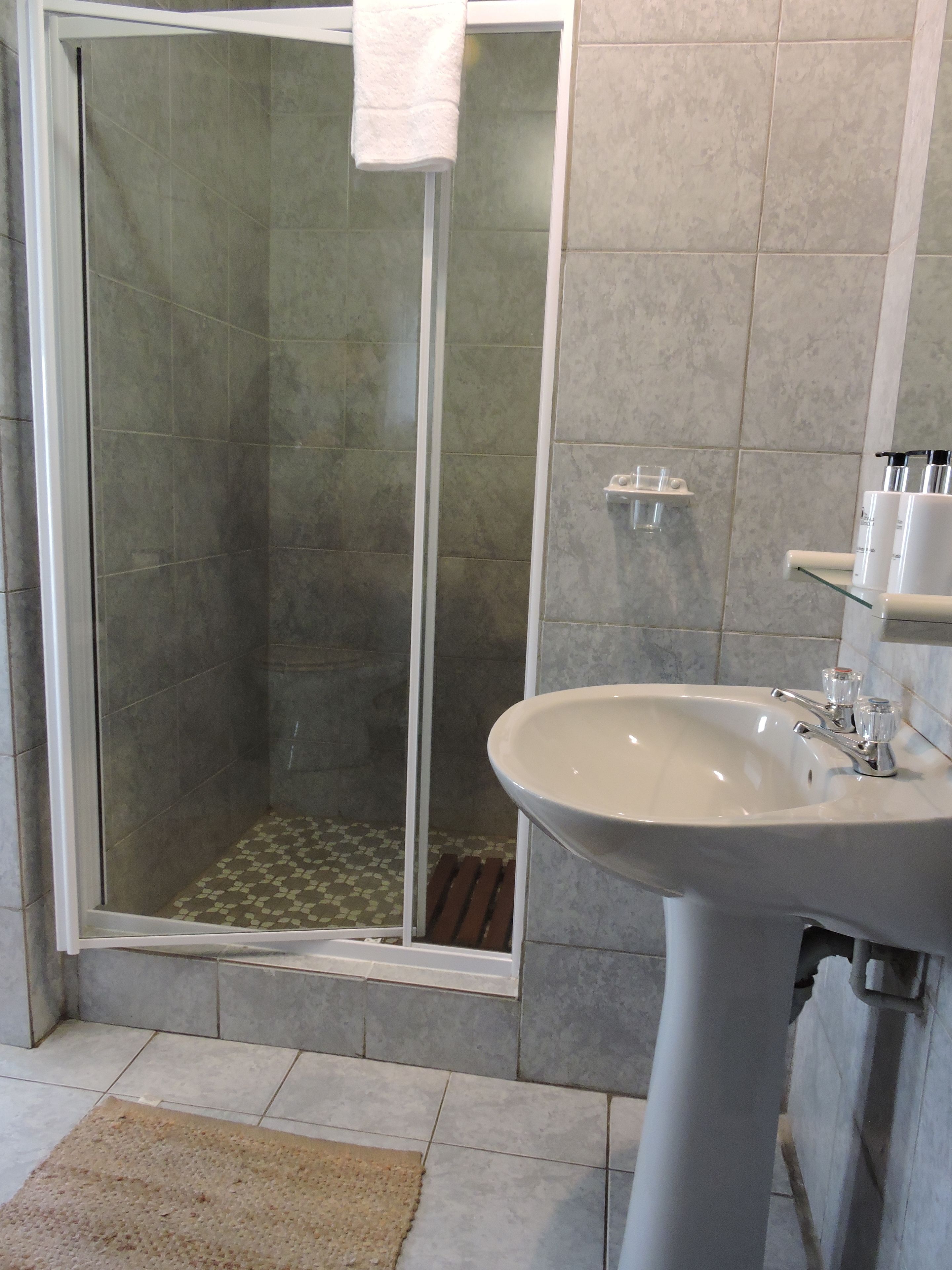 Une salle de bain avec une douche à parois de verre, un lavabo avec un miroir et un sol carrelé.