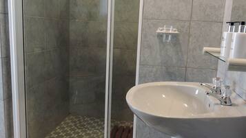 Une salle de bain avec une douche à parois de verre, un lavabo avec un miroir et un sol carrelé.