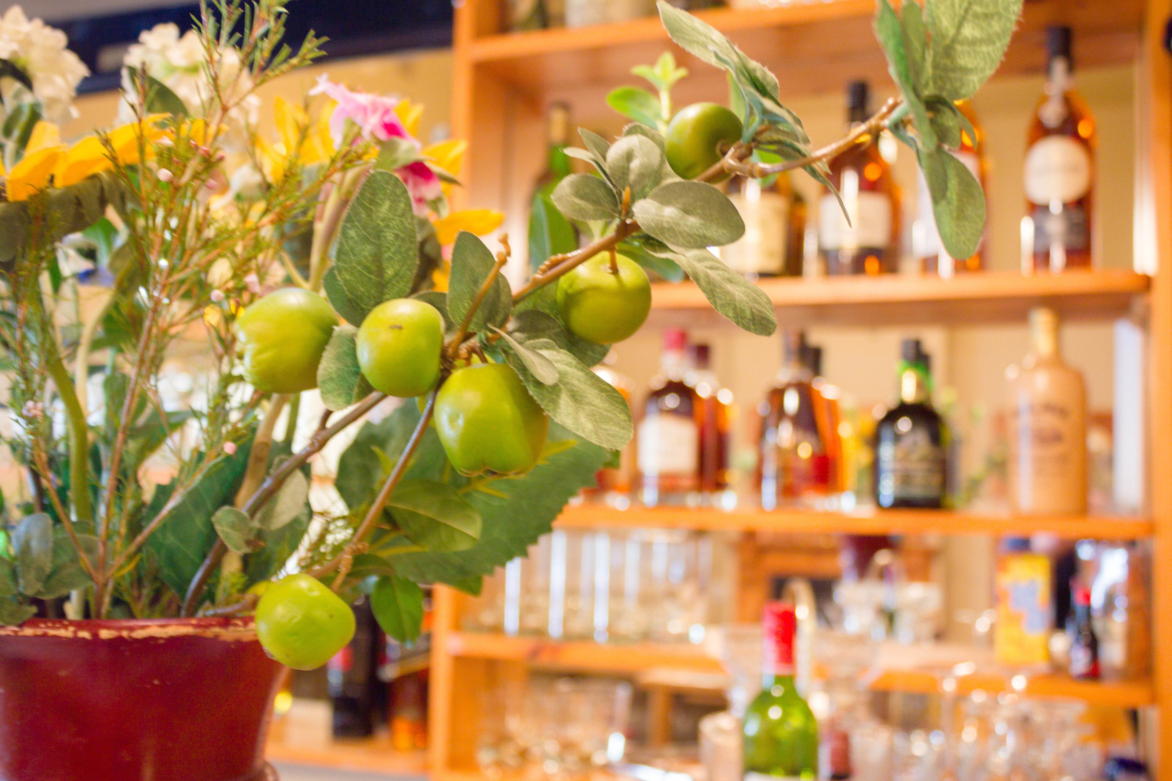 A potted plant with green apples and leaves in a store with shelves of bottles and glasses in the background.