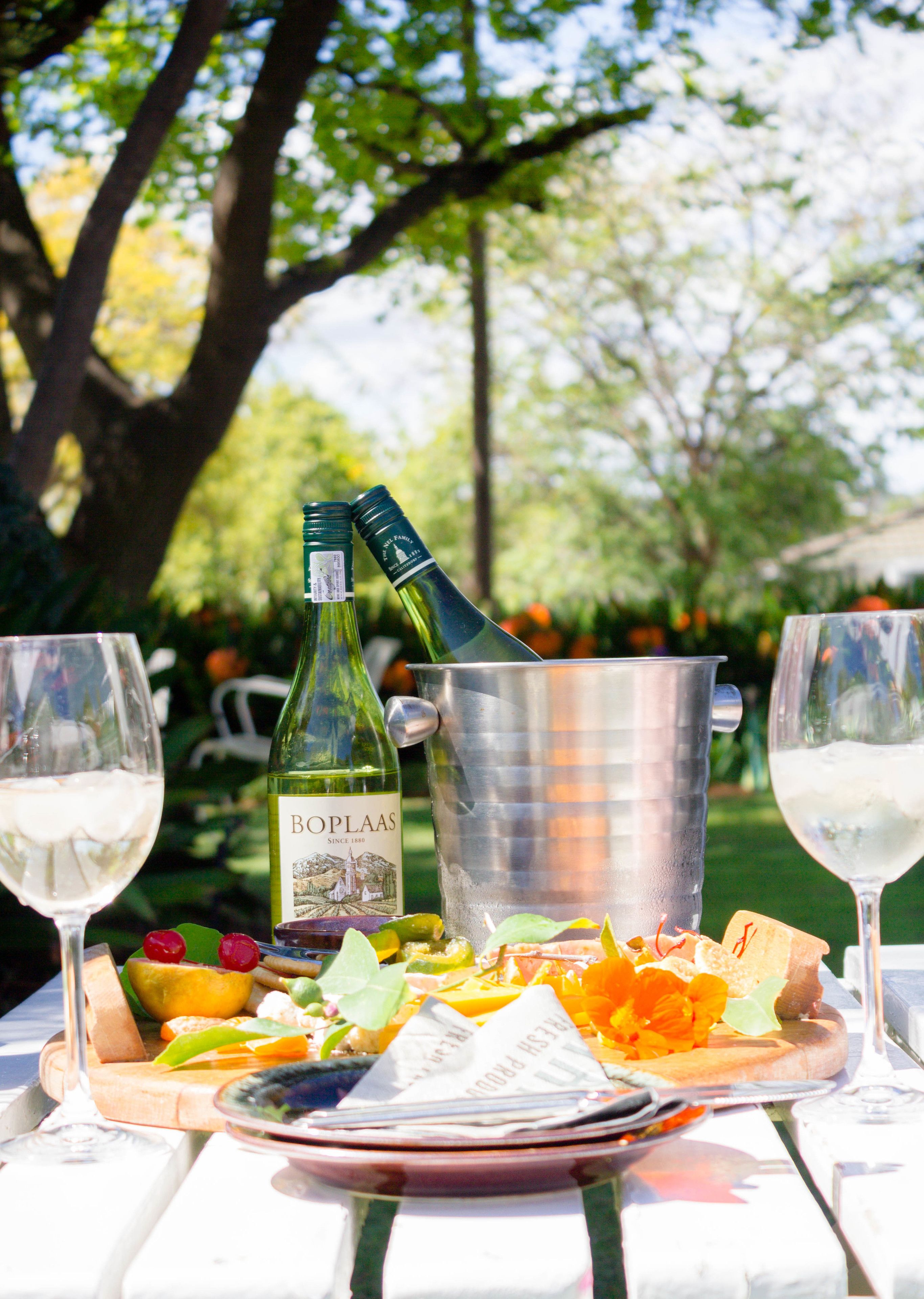 Une table avec une bouteille de vin BoPlaas, un seau en métal et des verres de vin blanc.