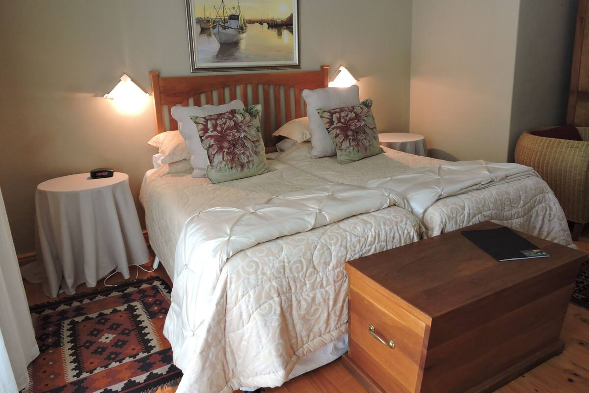 A double bed with a wooden headboard, two bedside tables with lamps, a nightstand, and a wooden chest of drawers.