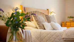 Una cama bien hecha con un cabecero de madera, una mesita de noche con una lámpara y un jarrón con flores en el suelo.