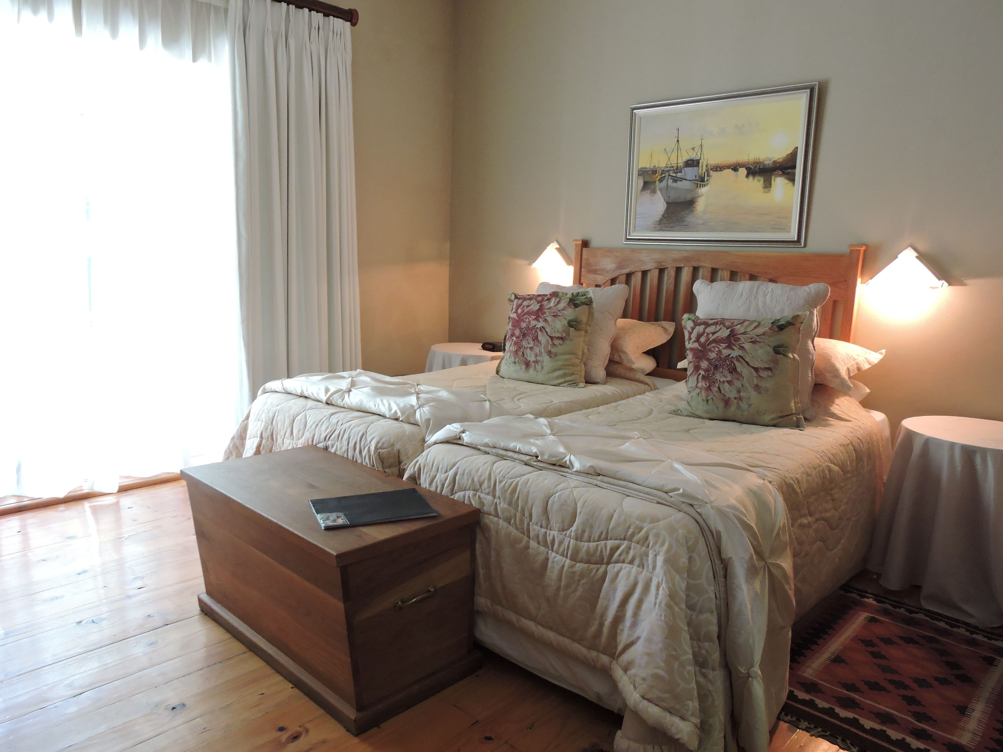 A double bed with floral pillows, a bedside table, a nightstand, a wooden bedside table, and a painting on the wall.