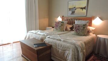 A double bed with floral pillows, a bedside table, a nightstand, a wooden bedside table, and a painting on the wall.