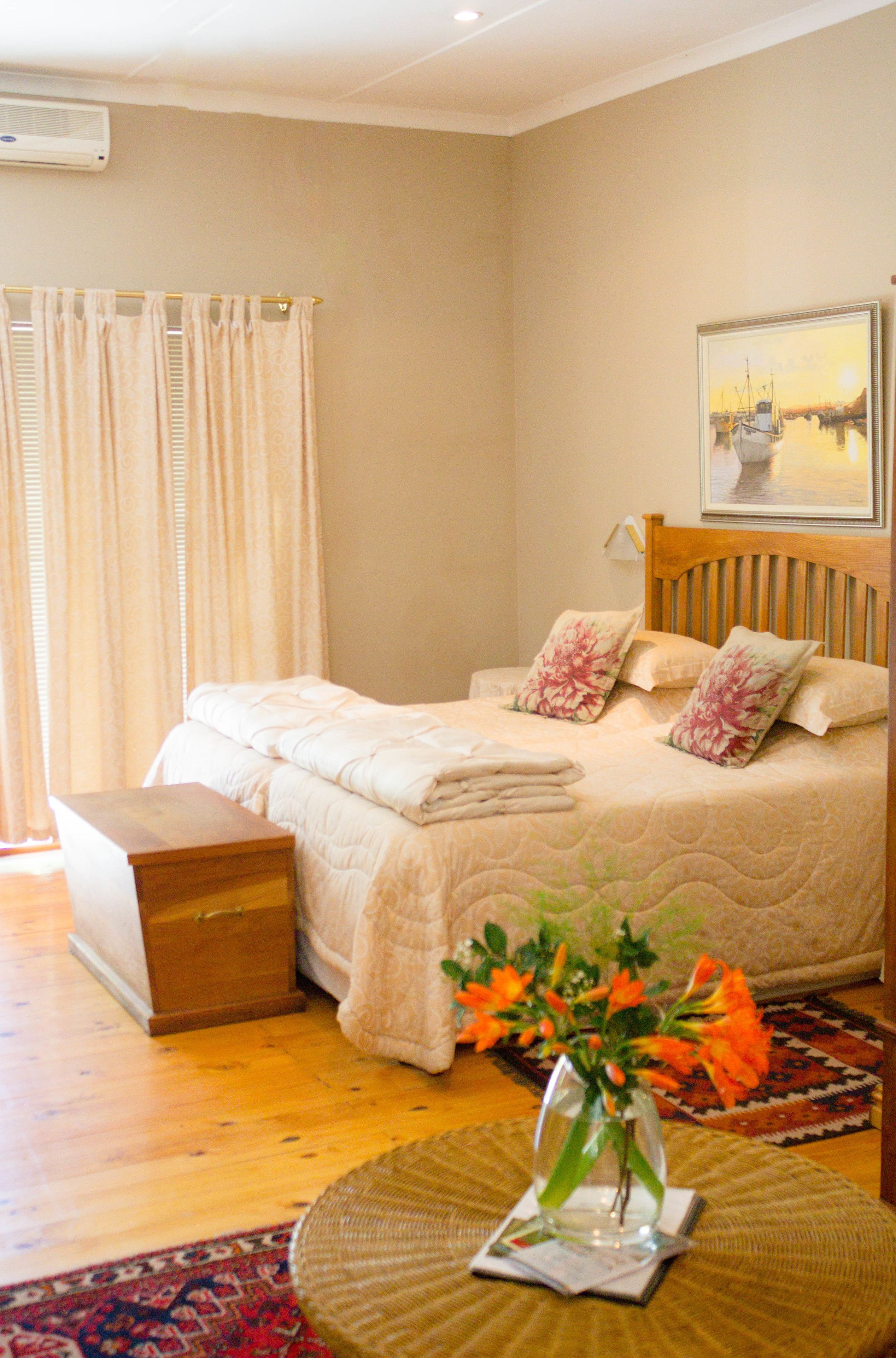 A bedroom with a bed, a wooden headboard, a nightstand, a bedside table, a vase with flowers, and a painting on the wall.
