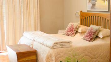 A bedroom with a bed, a wooden headboard, a nightstand, a bedside table, a vase with flowers, and a painting on the wall.